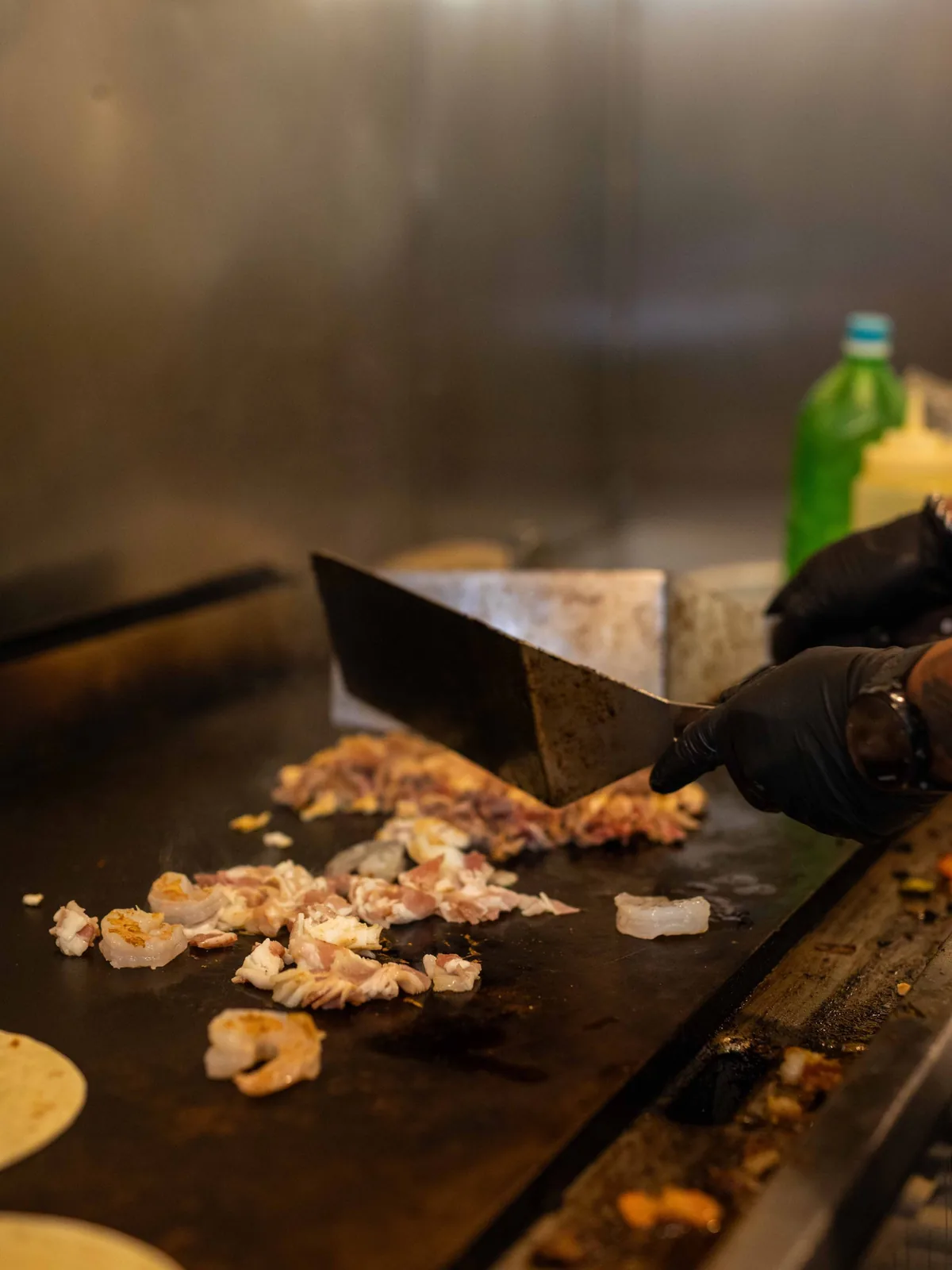 Cook chopping grilled chicken and shrimp on the flat-top grill in the Las Flores kitchen