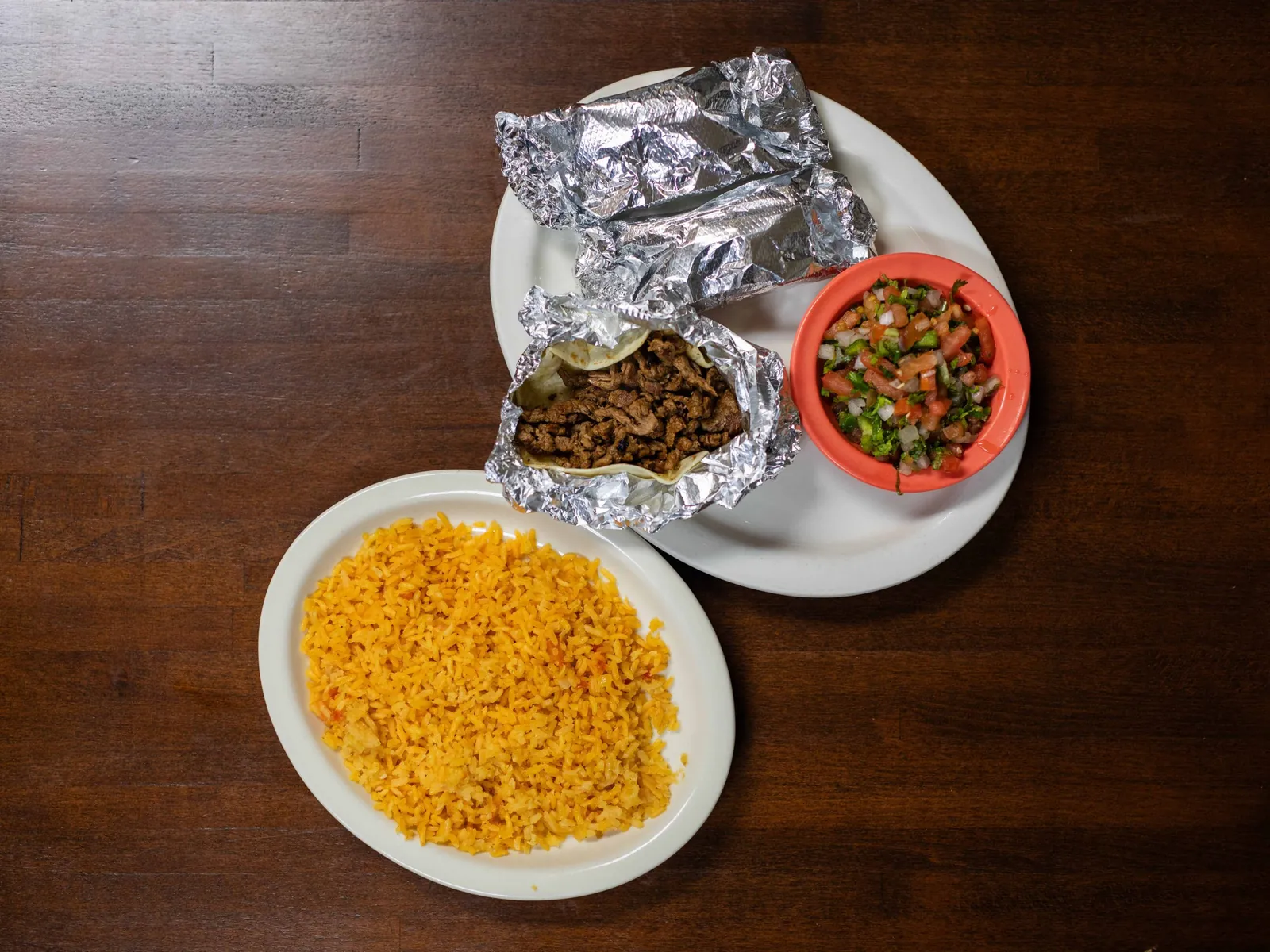 Tacos wrapped in foil with pico de gallo and Mexican rice on a wooden table